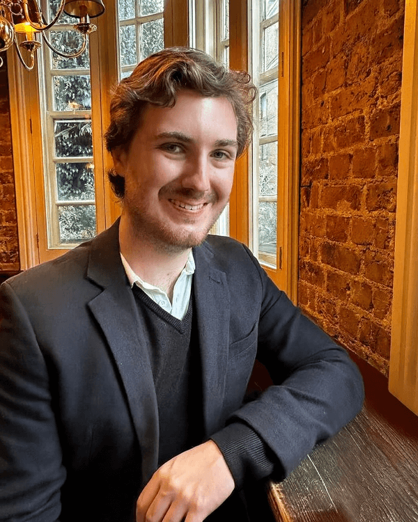 A picture of Maximilian Holder smiling, looking towards the camera, he is wearing formal attire.